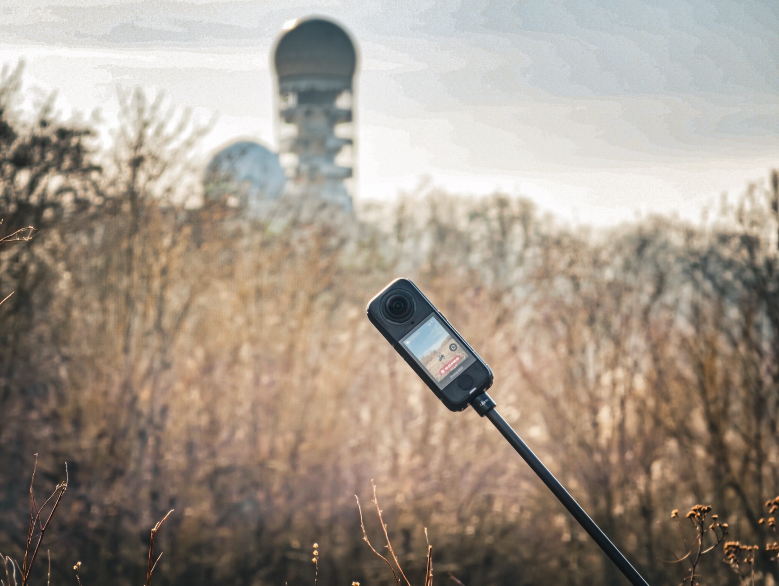Insta360 X4 Air 360-Grad-Kamera auf einem Selfiestick, im Hintergrund unscharf die Radarkuppel des Teufelsbergs in Berlin