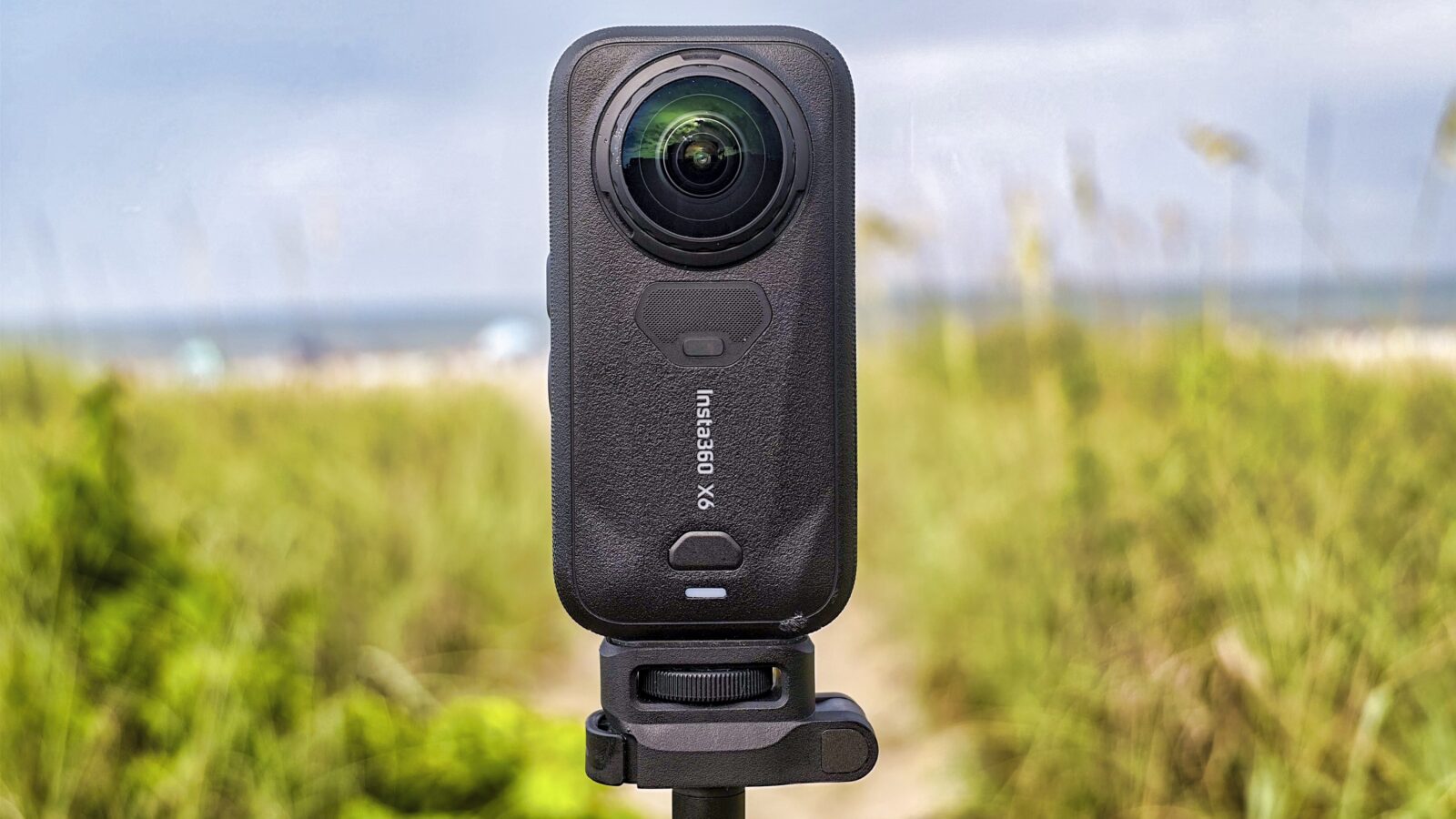 Die Insta360 X6 steht aufrecht im Sand, dahinter Meer und Himmel