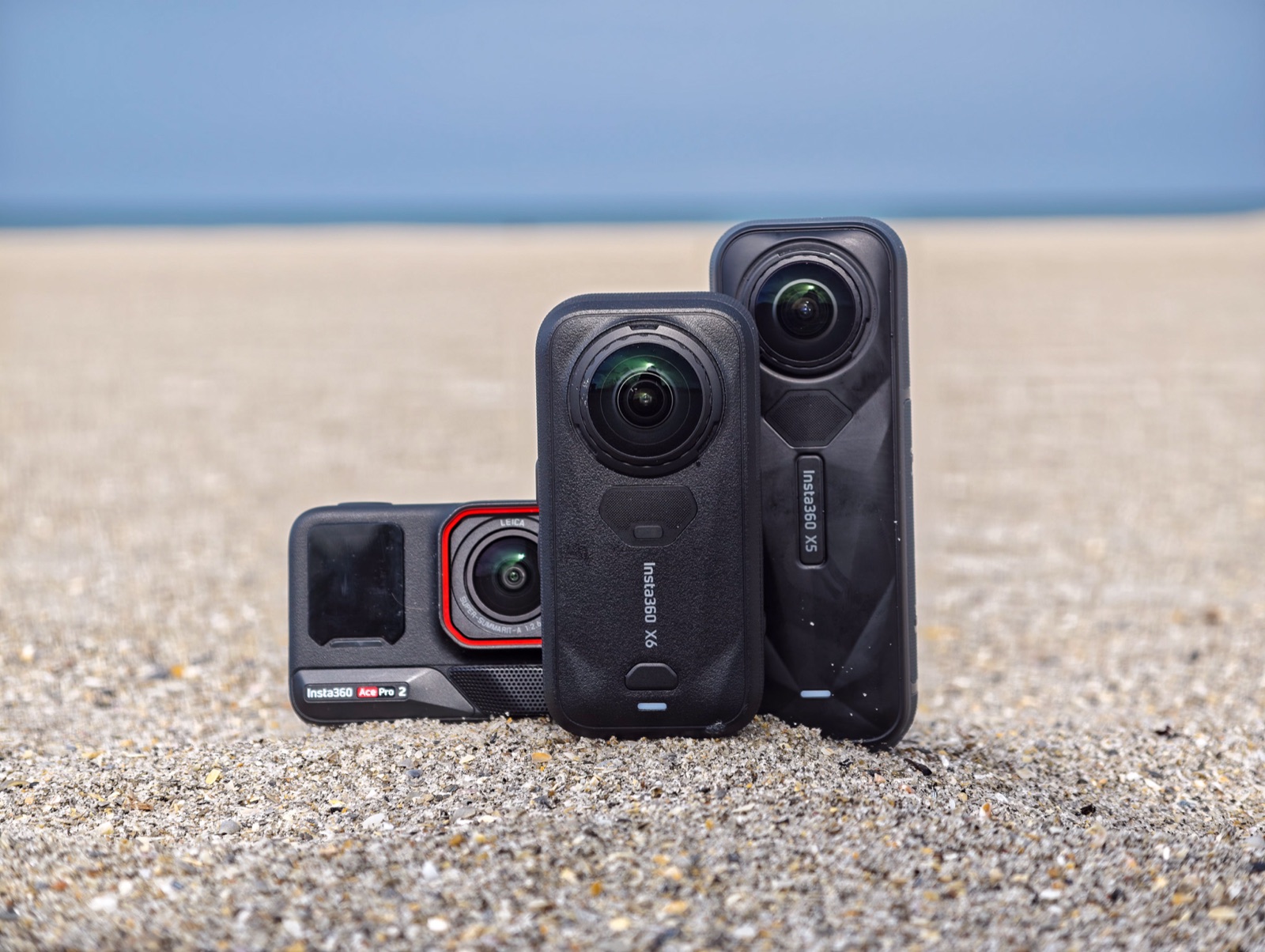 Insta360 Ace Pro 2, X6 und X5 nebeneinander im Sand am Strand — Größenvergleich der drei Kameras